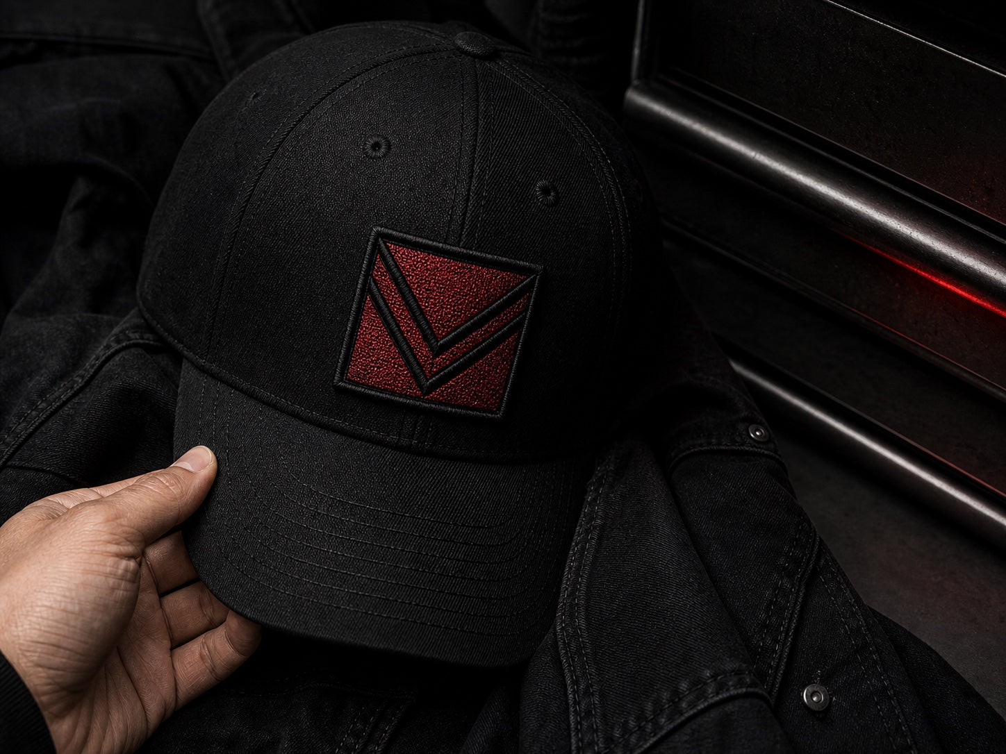 Hand holding a black Vortray cap with a red embroidered patch